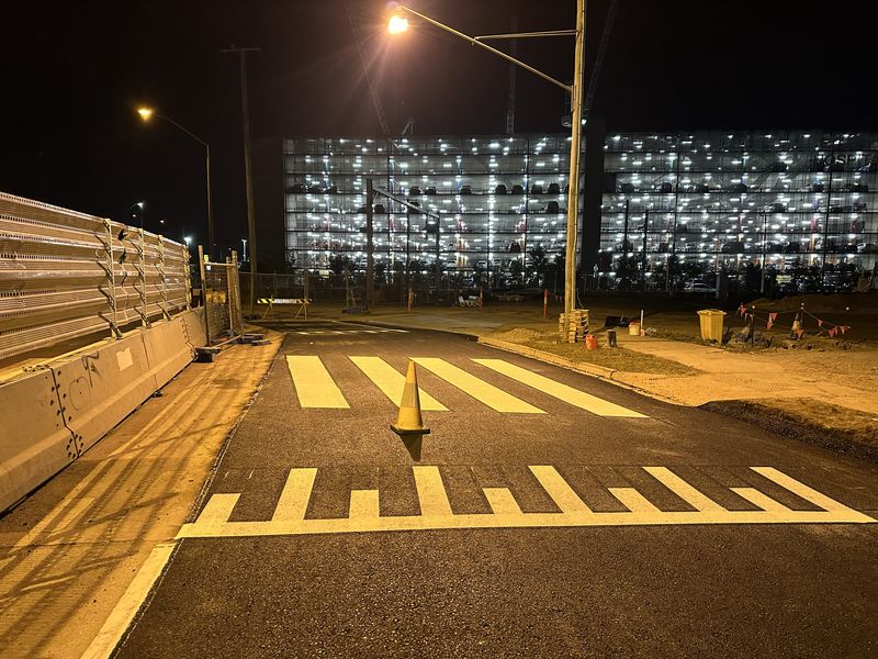 White pedestrian crossing and piano key markings on a road beside a car park building in Logan